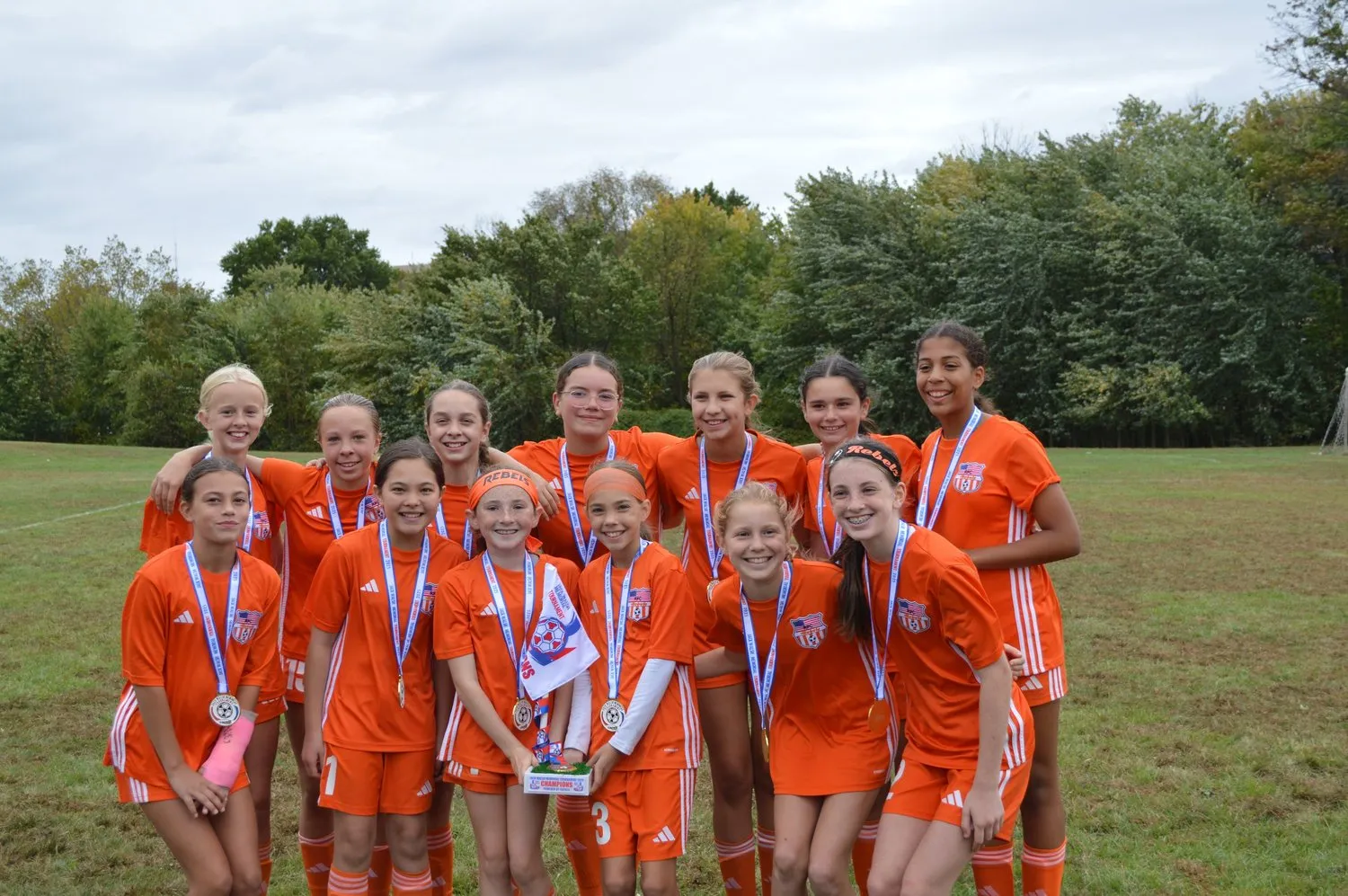 A Rebels girls team in orange with their medals and banner after winning the 2013 Jack Walsh Tournament